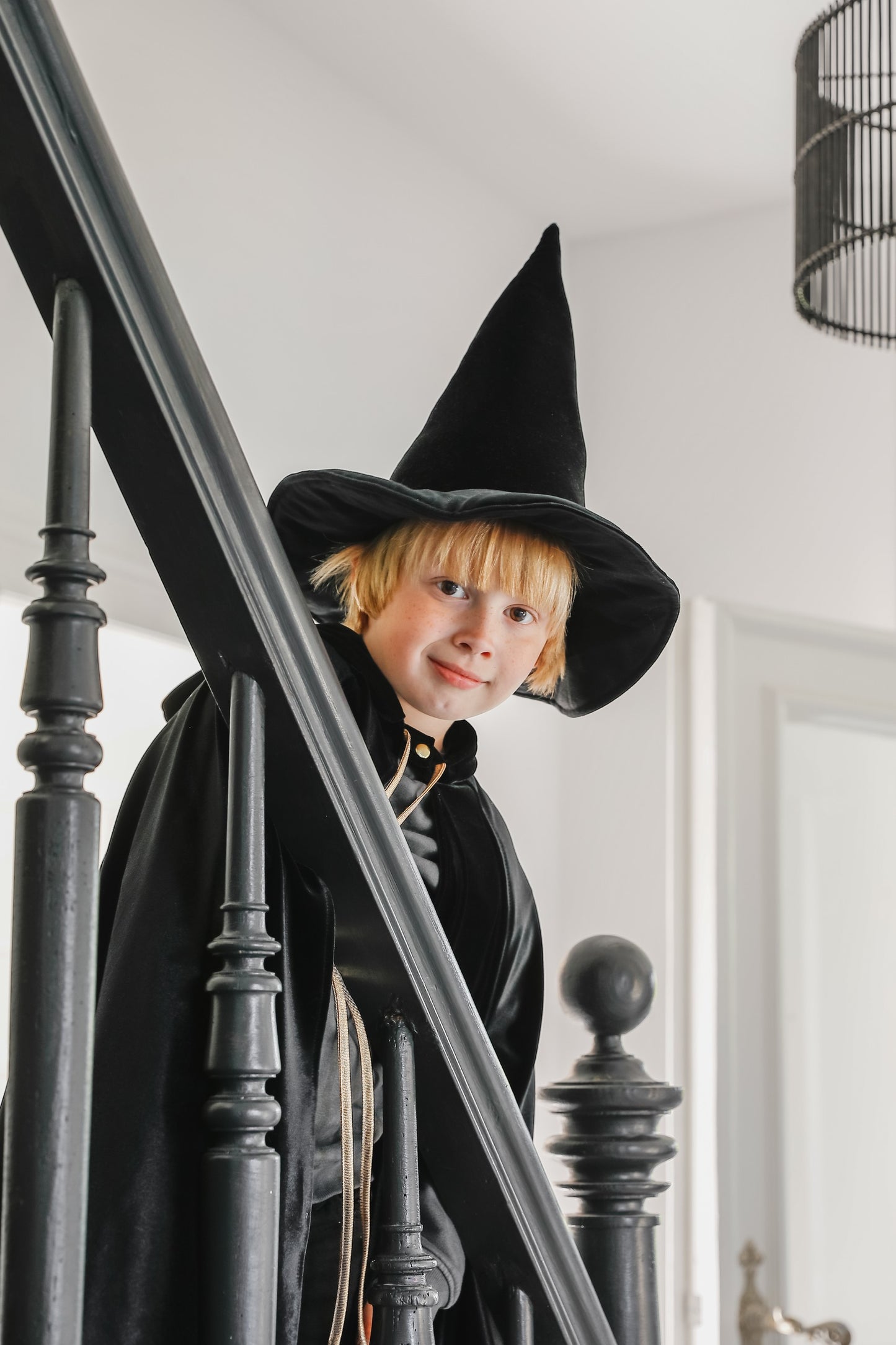 Moi Mili Black Magic Cape: a child in a flowing velvet costume climbing the wooden stairs of a cozy family home