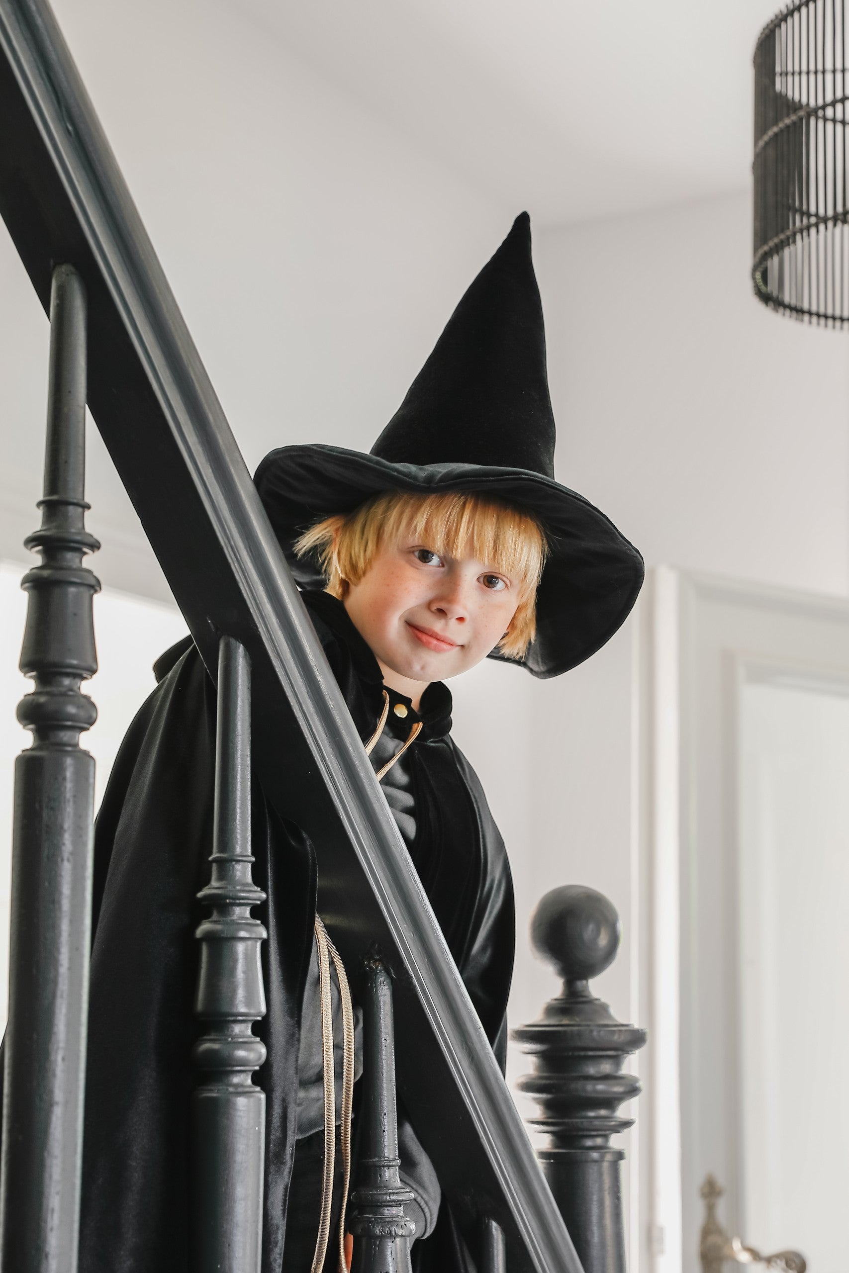Moi Mili Black Magic Cape: a child in a flowing velvet costume climbing the wooden stairs of a cozy family home