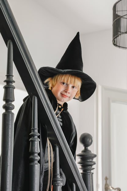 Moi Mili Black Magic Cape: a child in a flowing velvet costume climbing the wooden stairs of a cozy family home