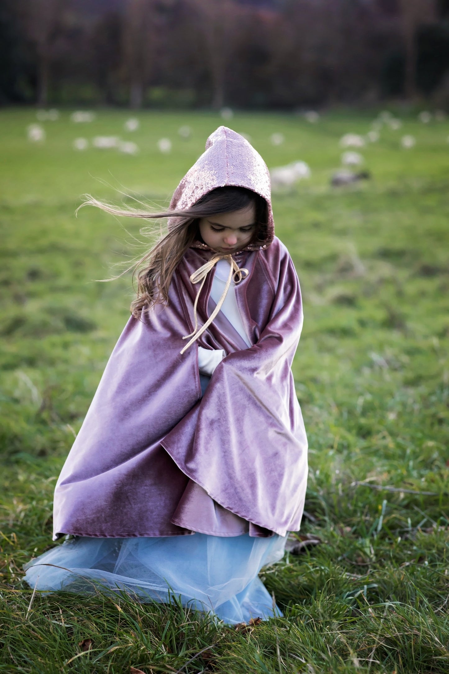 A young girl in a flowing Magic Cape Cosmic Pearl by Moi Mili catching the wind in a sunny natural landscape