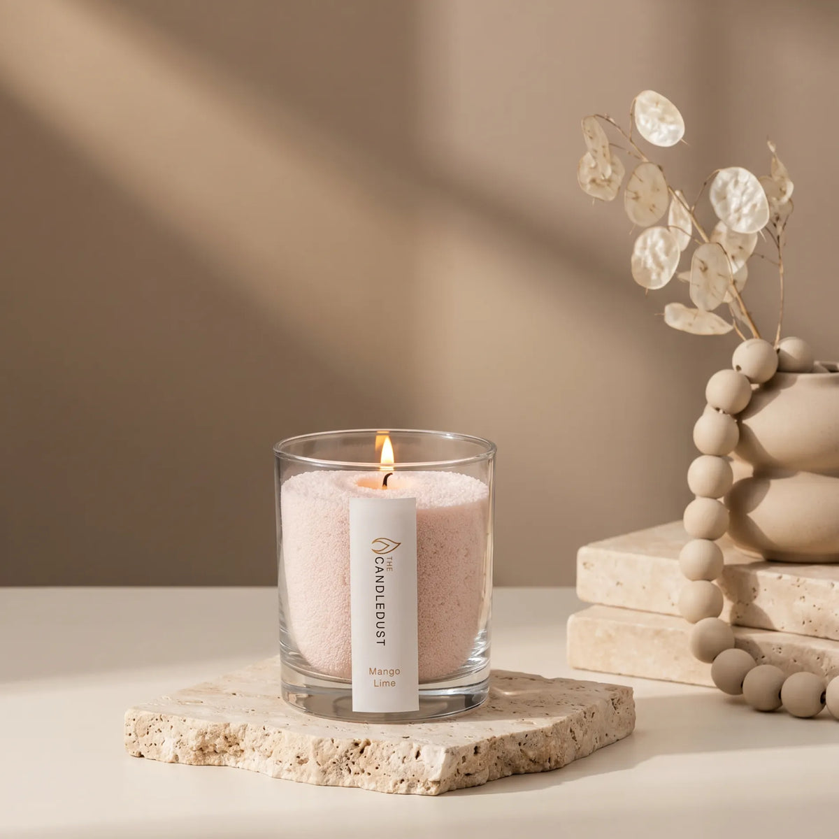 Lit Candledust Mango Lime scented pearled candle in a 160g glass jar sits on a stone slab on a tabletop