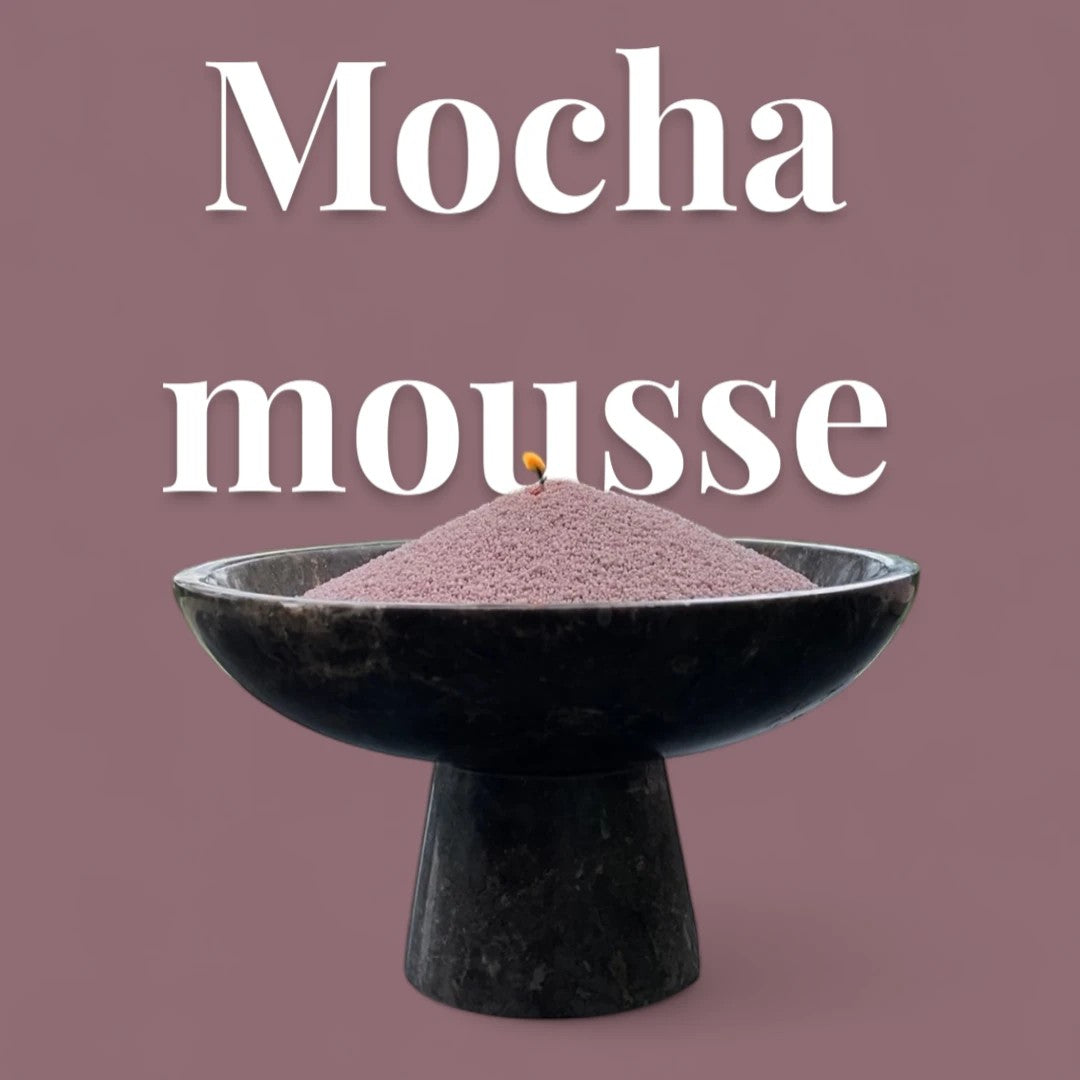 Mocha Mousse text on a matching warm mocha brown background with a glass vase full of unlit pearled candle sand in the foreground