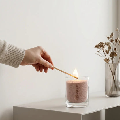 Woman's hand lighting the cotton wick of a Nude unscented pearled sand candle in glass
