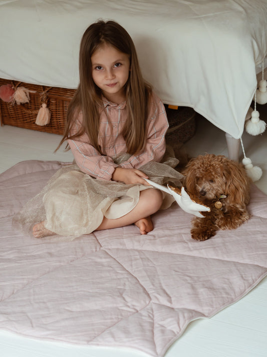 Moi Mili Powder Pink Linen Leaf Playmat: a toddler girl sitting with a small puppy on a soft, quilted leaf-shaped baby mat