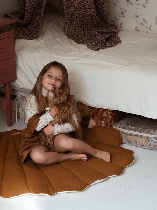 Moi Mili Caramel Shell Playmat: a toddler girl cuddling a small dog on a soft quilted linen shell-shaped baby mat