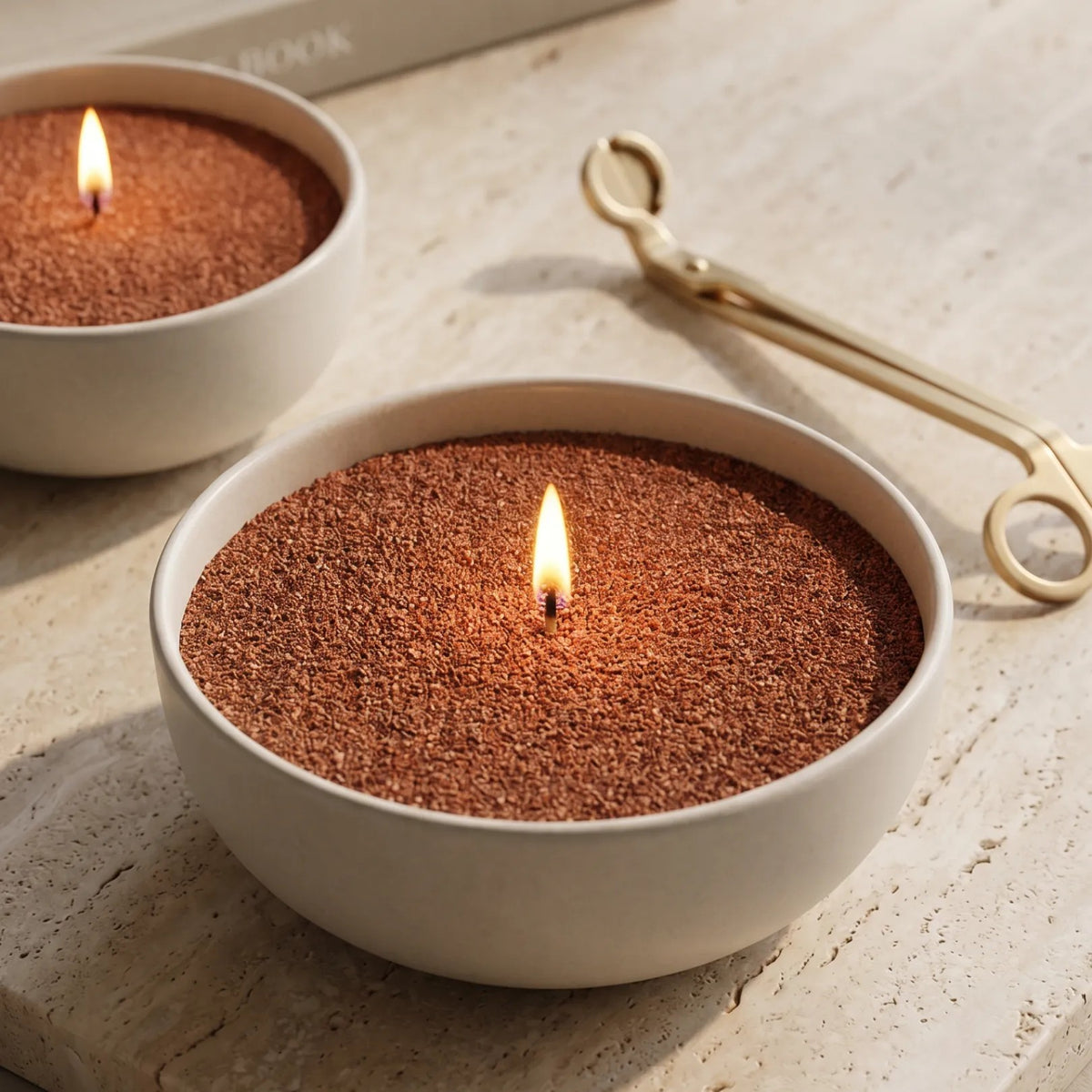  Elegant ceramic bow filled with Pecan pearled candle sand and lit cotton wicks resting on a refined marble countertop