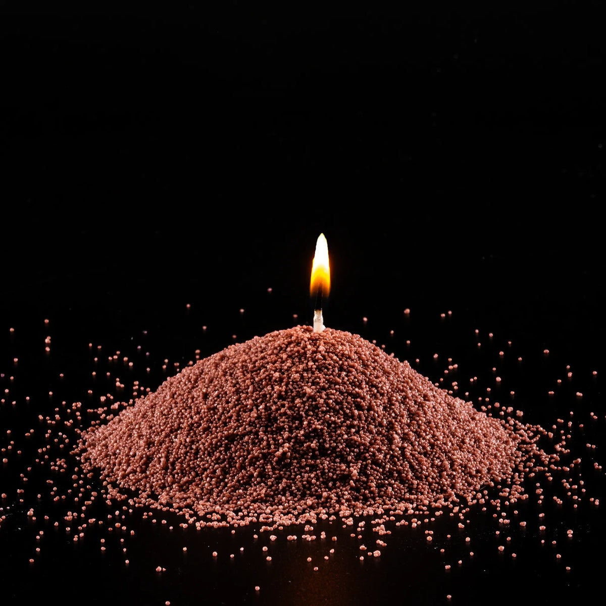 Burning Pecan pearled sand candle with a bright flame isolated on a dramatic black background
