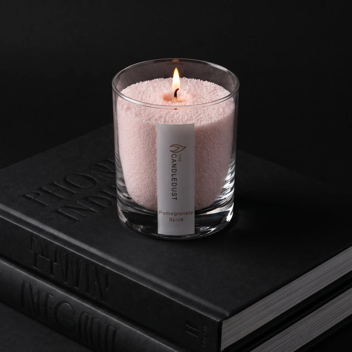 Lit Pomegranate Spice scented pearled glass candle resting on stacked books
