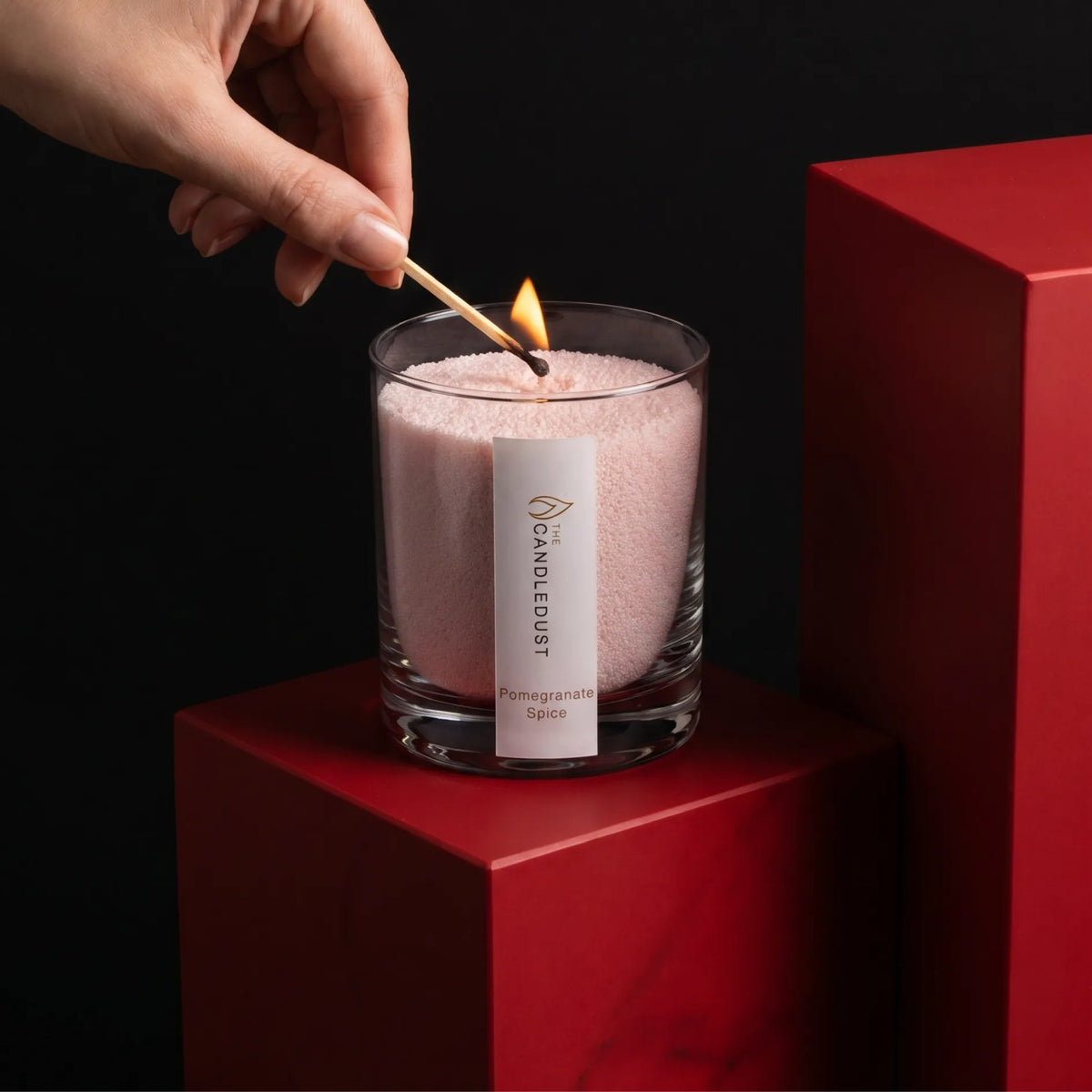 Close-up of a woman's hand lighting the cotton wick of a Pomegranate Spice scented pearled sand candle in glass
