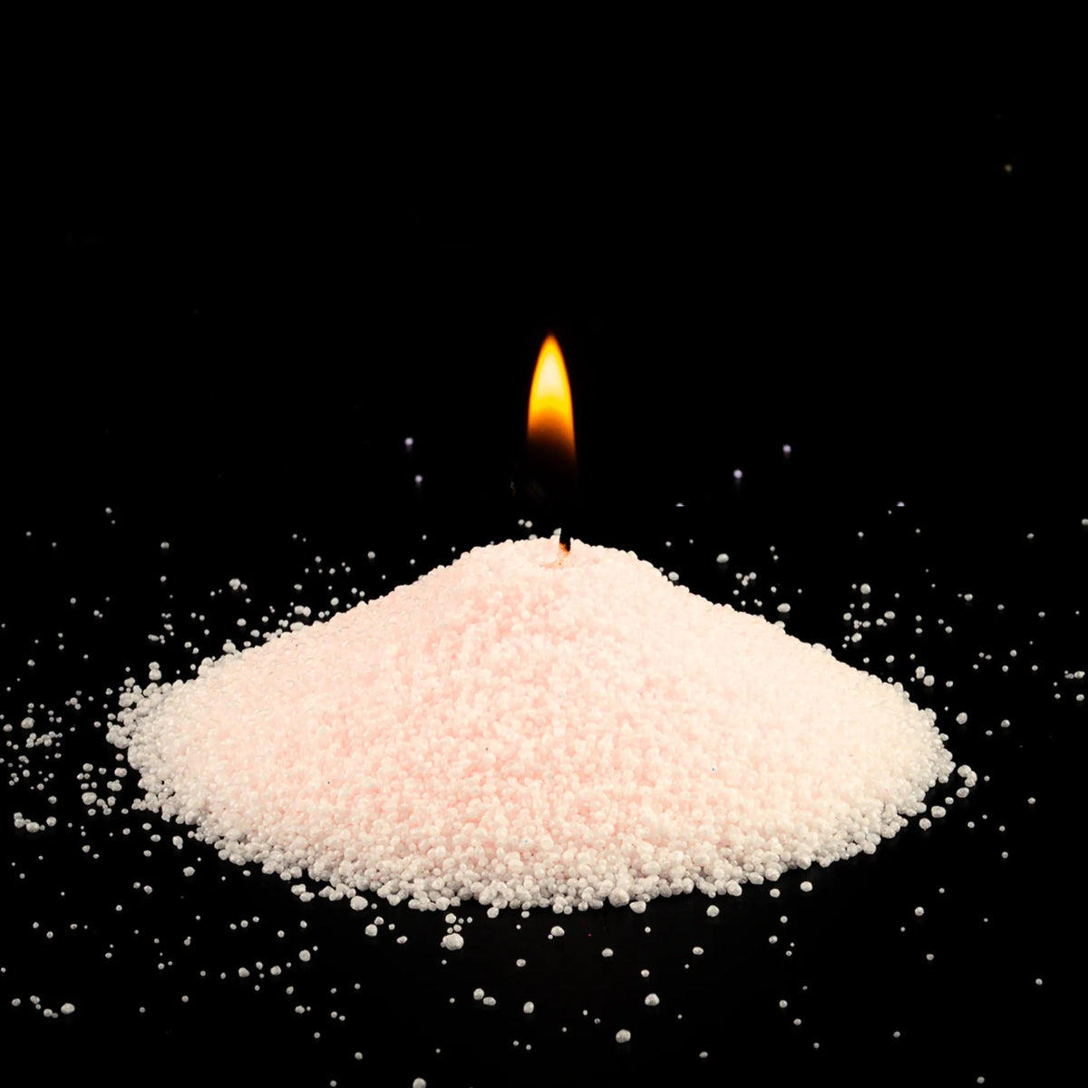 Burning Pomegranate Spice scented pearled sand candle with a bright flame isolated on a dramatic black background