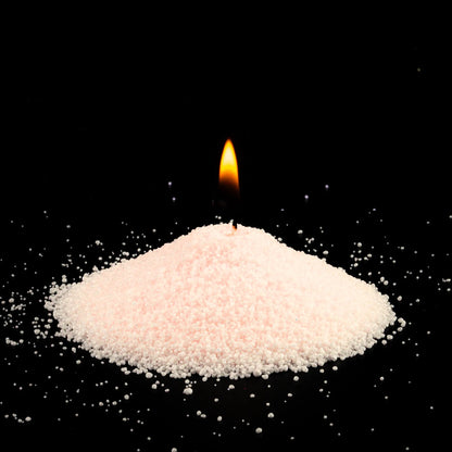 Burning Pomegranate Spice scented pearled sand candle with a bright flame isolated on a dramatic black background