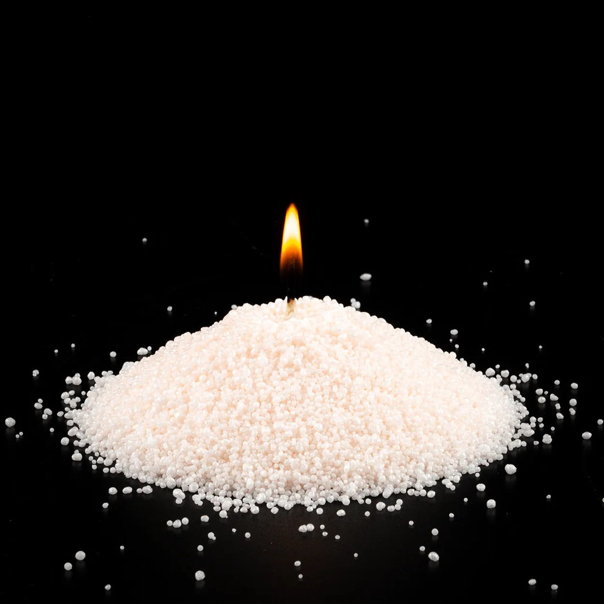 Burning Pumpkin Spice scented pearled sand candle with a bright flame isolated on a dramatic black background