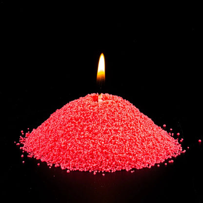 Burning Raspberry pearled sand candle with a bright flame isolated on a dramatic black background