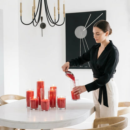 Woman filling decorative glass candle holders with Red natural pearled candle sand