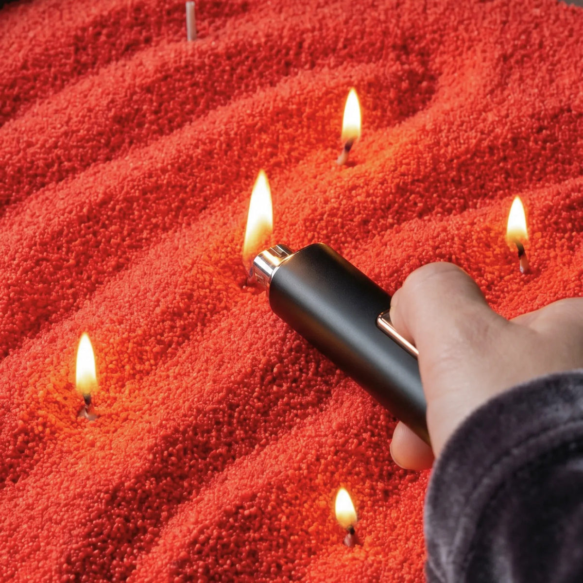 Close-up of a woman's hand lighting the cotton wick of a Red pearled sand candle
