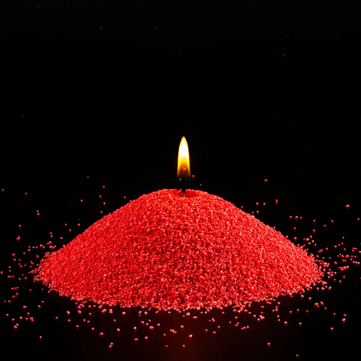 Burning Red pearled sand candle with a bright flame isolated on a dramatic black background