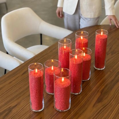 glass vases of various heights filled with burning Red pearled candle sand creating a glowing cluster on a wooden table