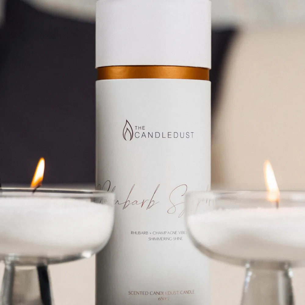 Candledust Rhubarb Sparkle scented pearled candle sand in a 650g cylinder tube branding in front of lit candles.