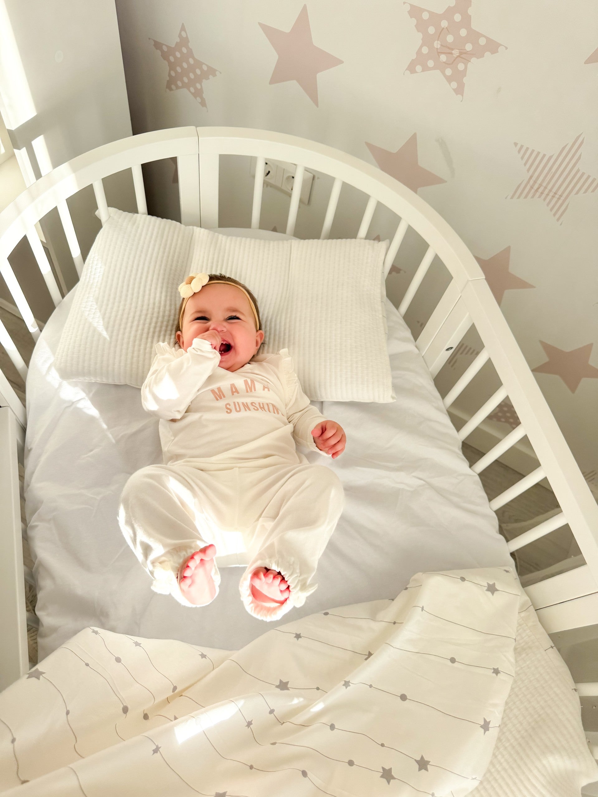 baby laying inside the round Baby Crib OLIN with Mattress - White in the sunny nursery