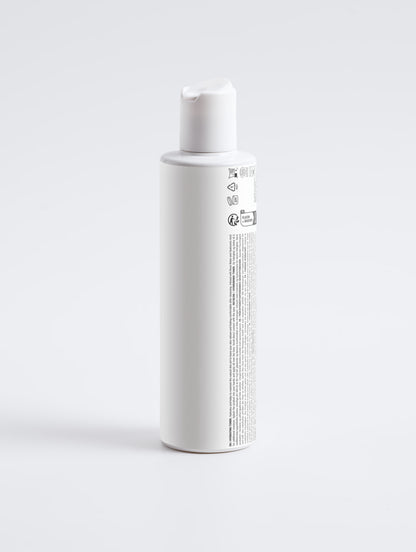 A tall, white cylindrical bottle with a matching white cap, shown from a side angle on a seamless light gray background. The bottle features a white label with black text and regulatory symbols.