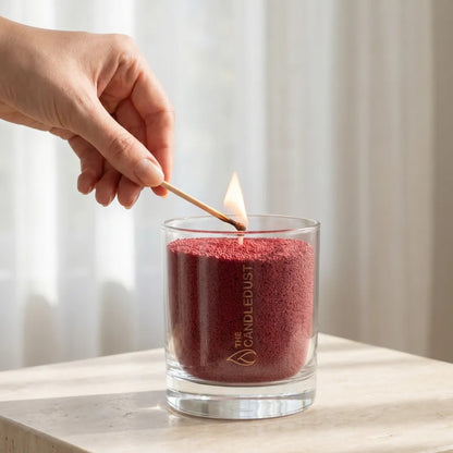 Close-up of a woman's hand lighting the cotton wick of a Sangria Red unscented pearled sand candle in glass