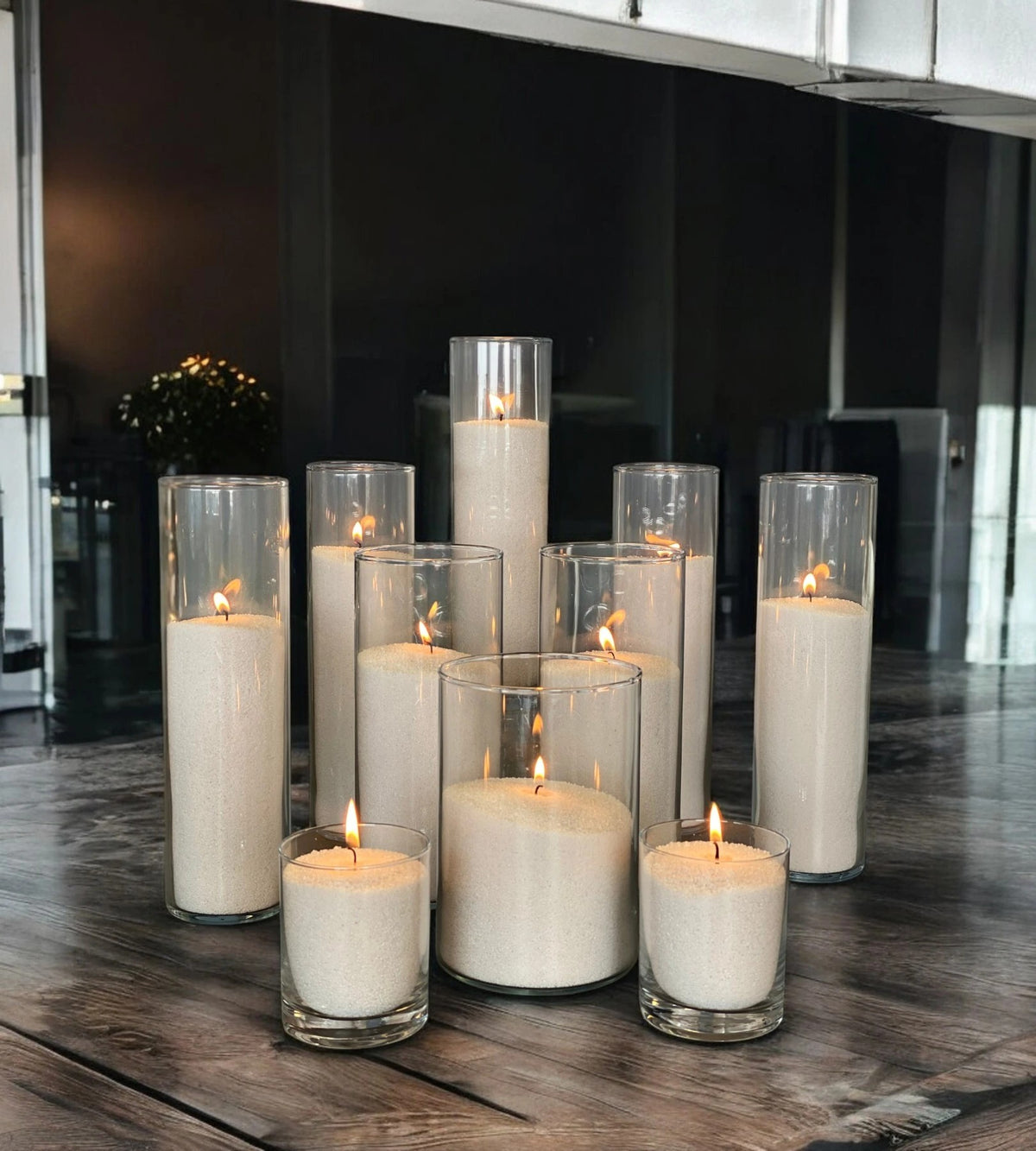Glass vases of various heights filled with burning Silver pearled candle sand creating a glowing cluster