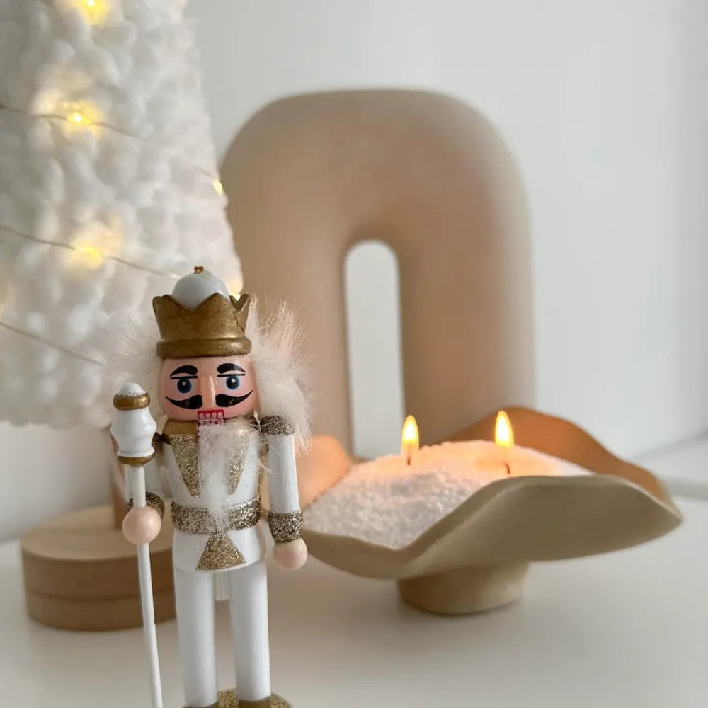 Decorative nutcracker figure with a crown in front of lit Candledust Silver unscented pearled candle sand