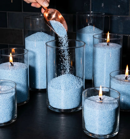 Close up of Woman's hand filling decorative glass candle holders with Sky Blue natural pearled candle sand
