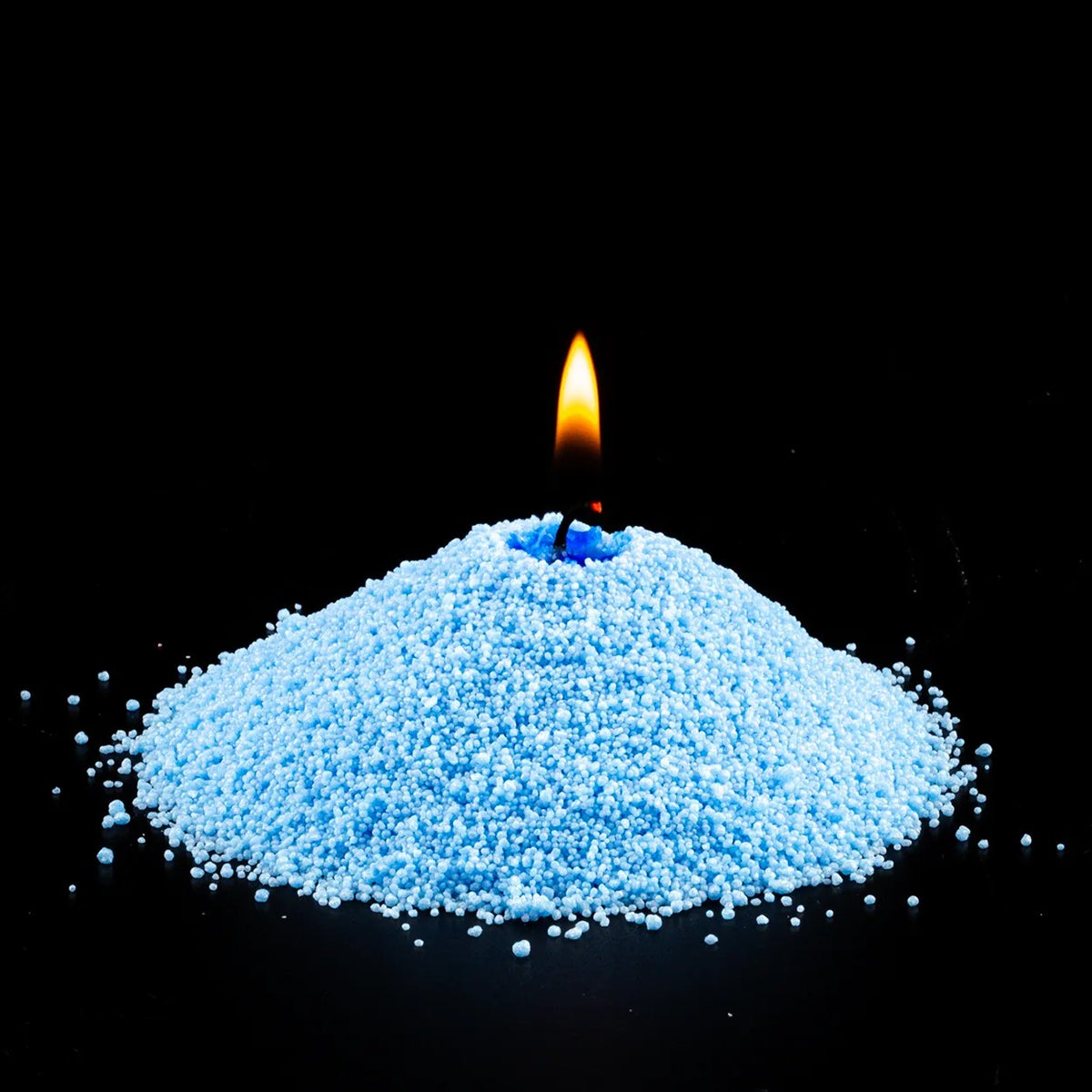 Burning Sky Blue pearled sand candle with a bright flame isolated on a dramatic black background