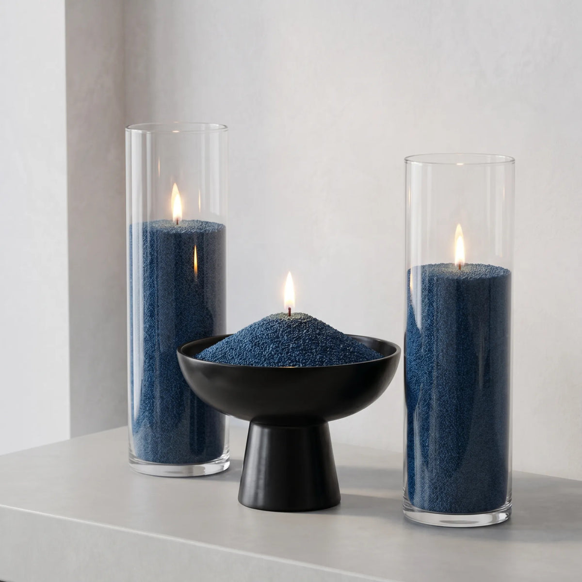 Three elegant glass vases of various heights filled with burning Space Grey pearled candle sand creating a glowing cluster