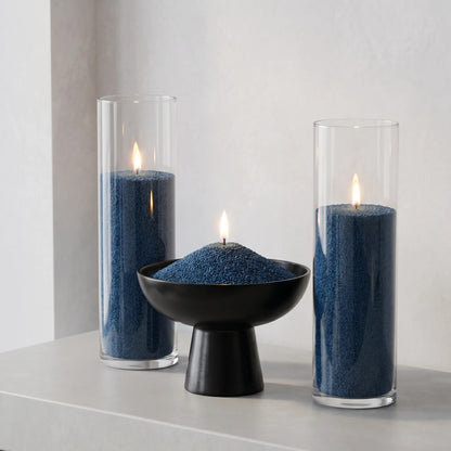 Three elegant glass vases of various heights filled with burning Space Grey pearled candle sand creating a glowing cluster