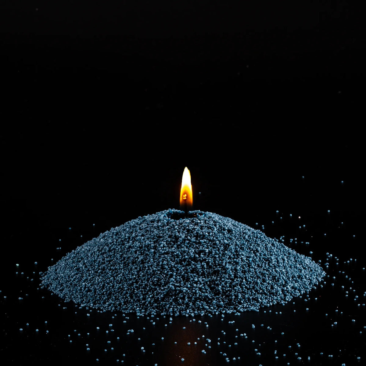 Burning Space Grey pearled sand candle with a bright flame isolated on a dramatic black background