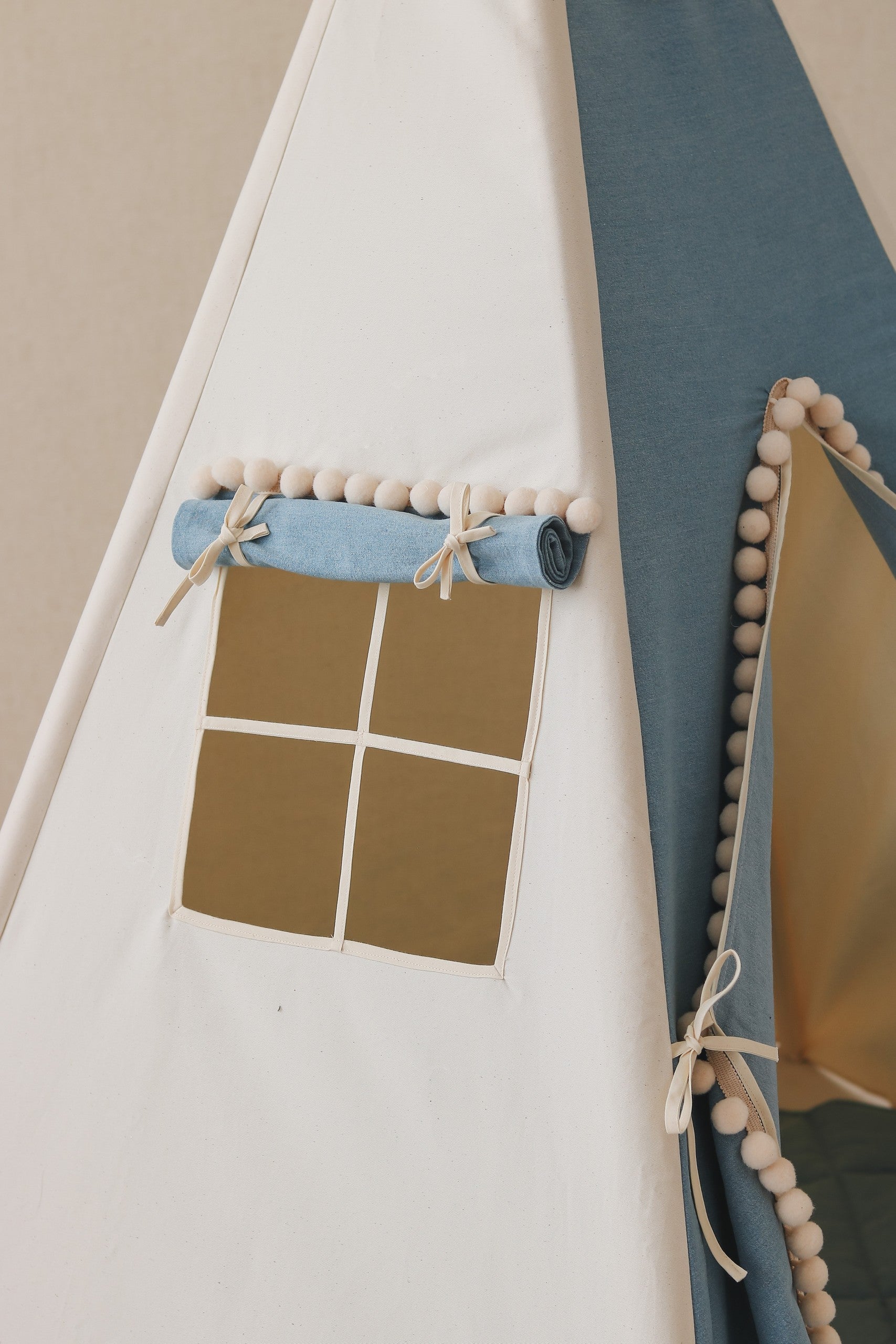 Nursery detail: close-up of the side window on a Moi Mili Jeans Teepee Tent, showing the contrast between blue denim and cream pompom trim