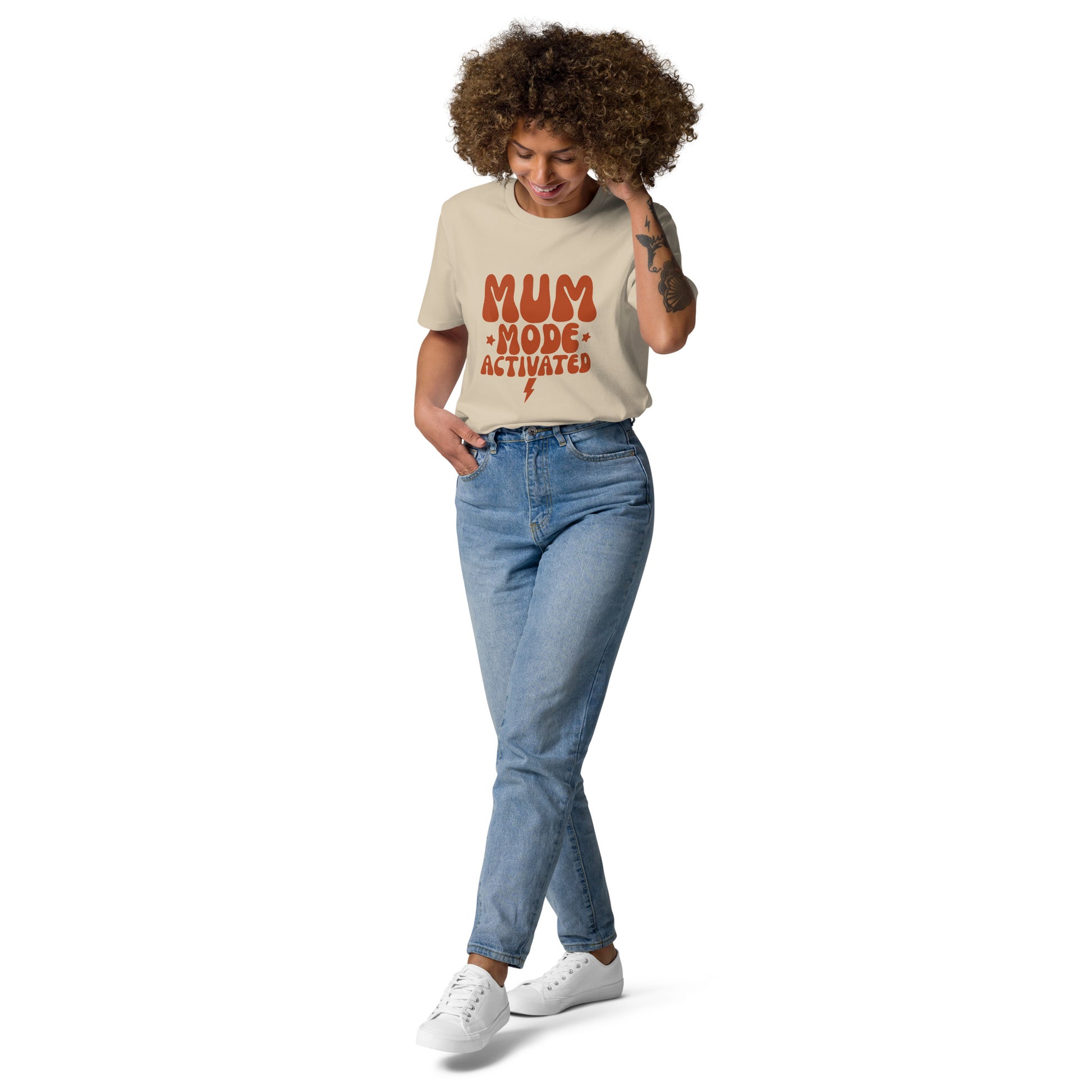 "A happy woman smiling while wearing a sand-colored organic cotton t-shirt with the retro terracotta MUM MODE ACTIVATED design.