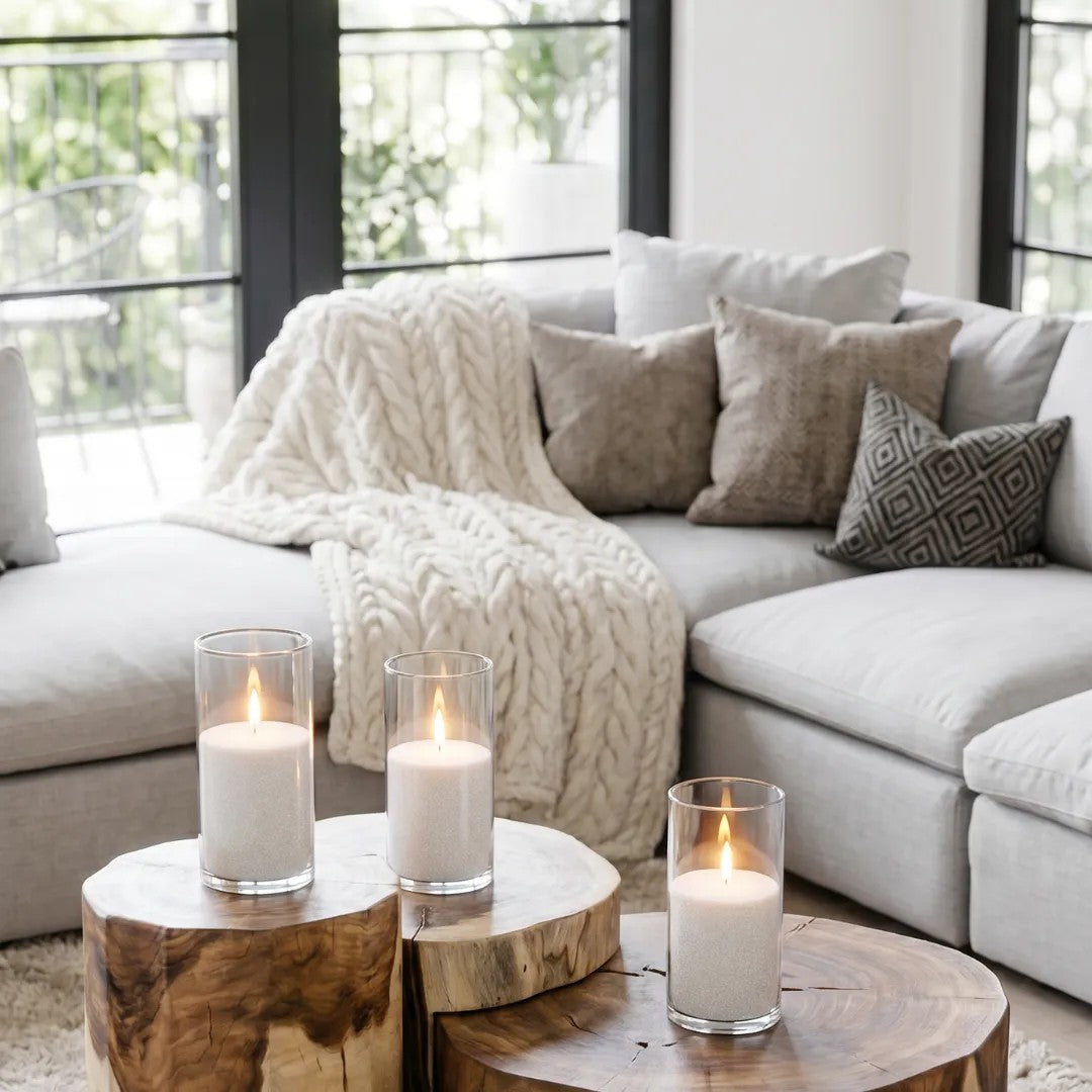 Three lit Candledust pearled sand candles in glass holders displayed on a solid wood coffee table in a bright living room