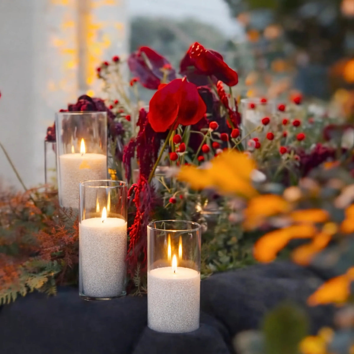 Glowing cluster of lit Candledust pearled sand candles in glass holders nestled amongst lush floral arrangements